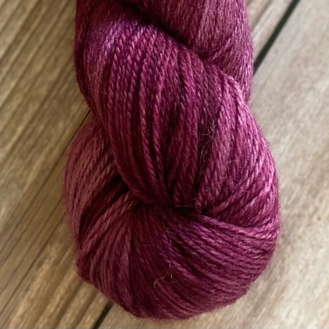 A skein of sparkly wool and nylon yarn hand dyed in the color  deep mauve