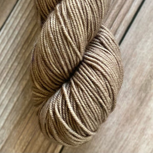 Skein of superwash merino yarn hand dyed in a tan color sitting against a wood background
