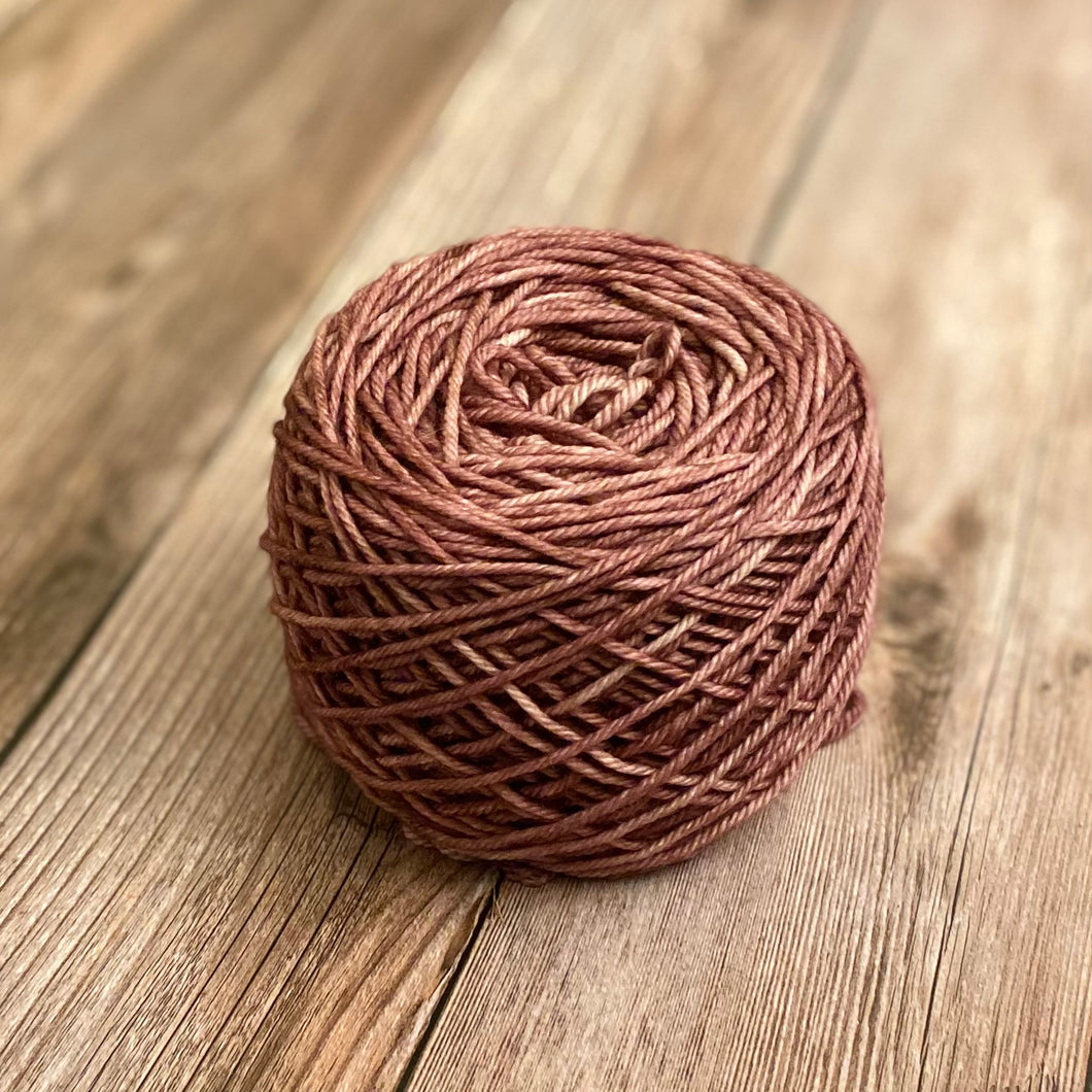 Image of mauve colored yarn wound into a caked-shape ball