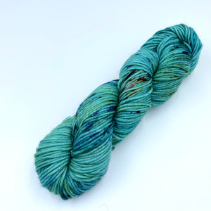 Skein of superwash merino yarn hand dyed with a turquoise base with blue and gold speckles