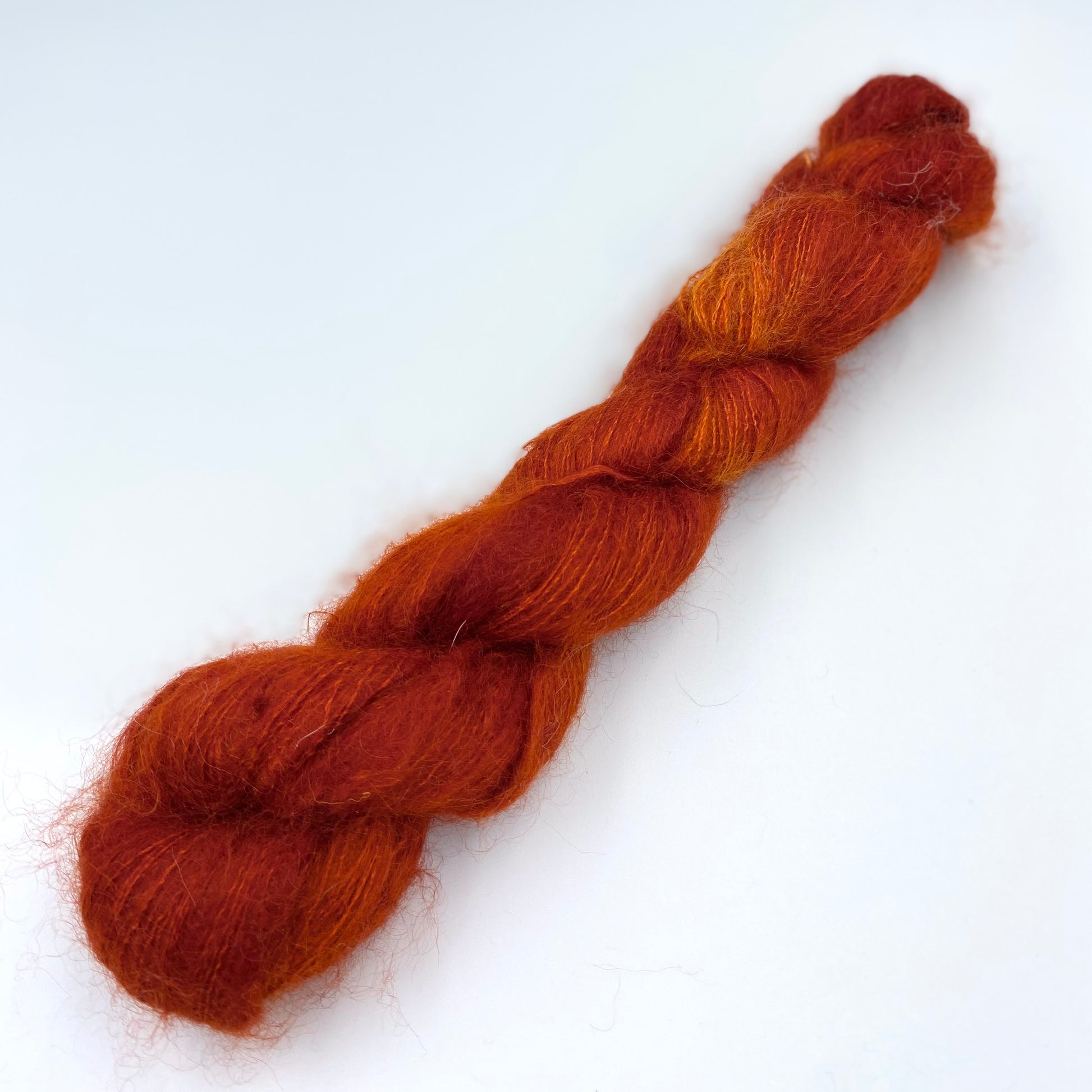 A skein of hand dyed kid mohair and silk yarn in a rust orange  color 