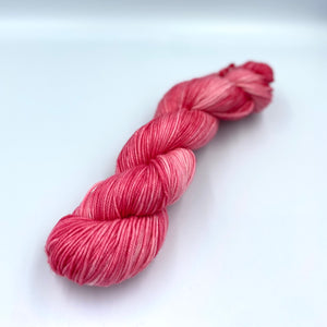 Skein of superwash merino yarn hand dyed in a strawberry pink color