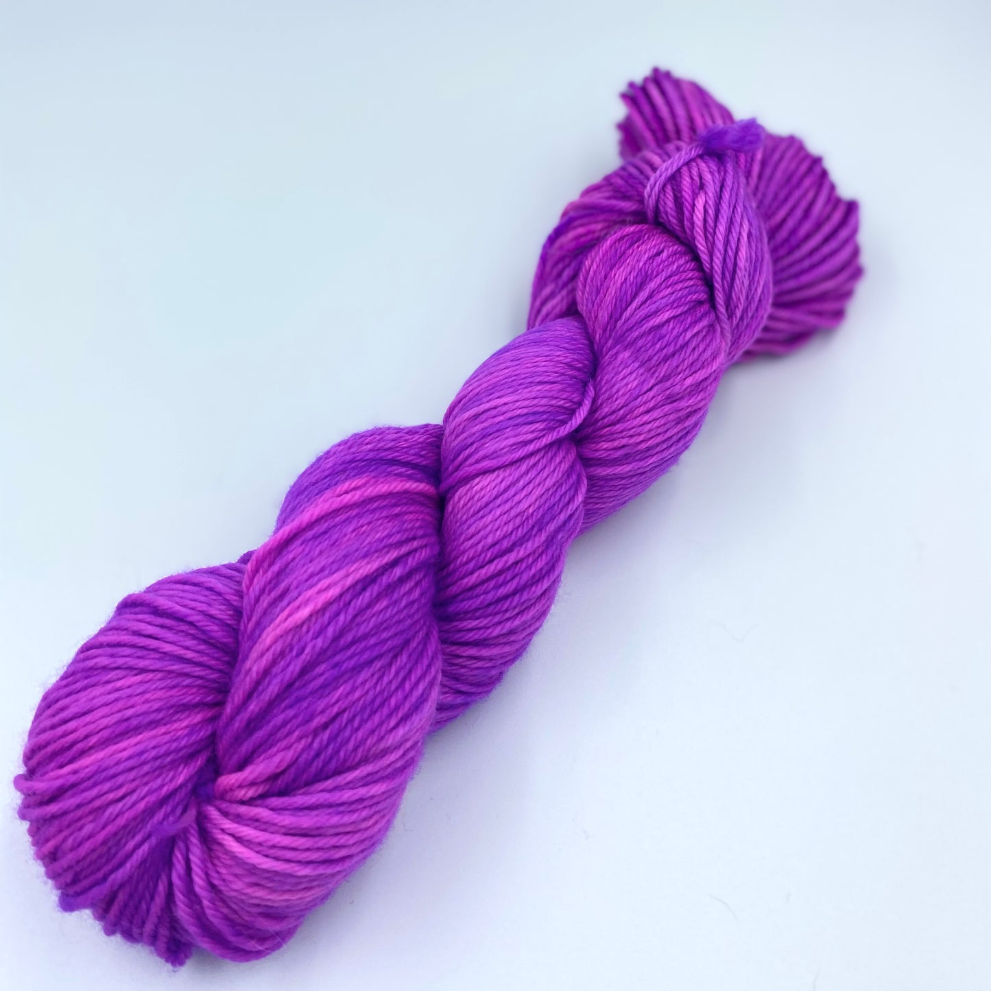 Skein of superwash merino yarn hand dyed in a purpleish pink color