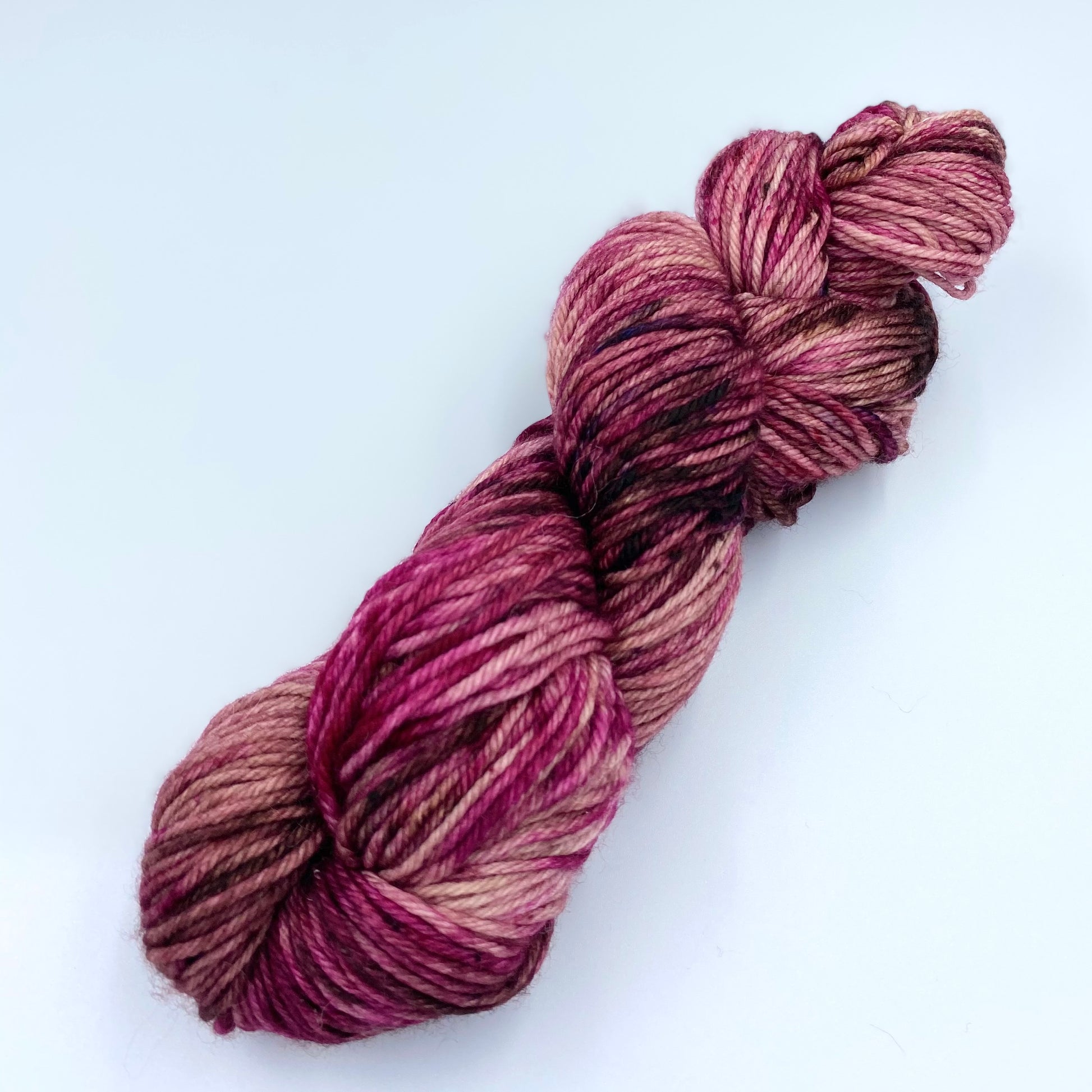 Skein of superwash merino yarn hand dyed in a mix of fuschia, brown, rose and baby pink color