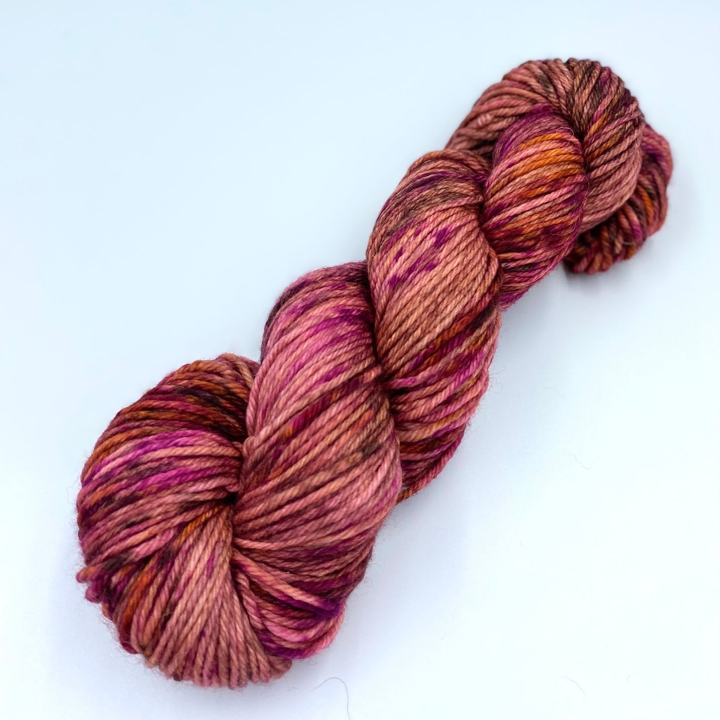 Skein of superwash merino yarn hand dyed in a mix of brown, golden, and fuschia color
