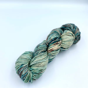 Skein of superwash merino yarn hand dyed with greens, blues and browns splashed on a white base