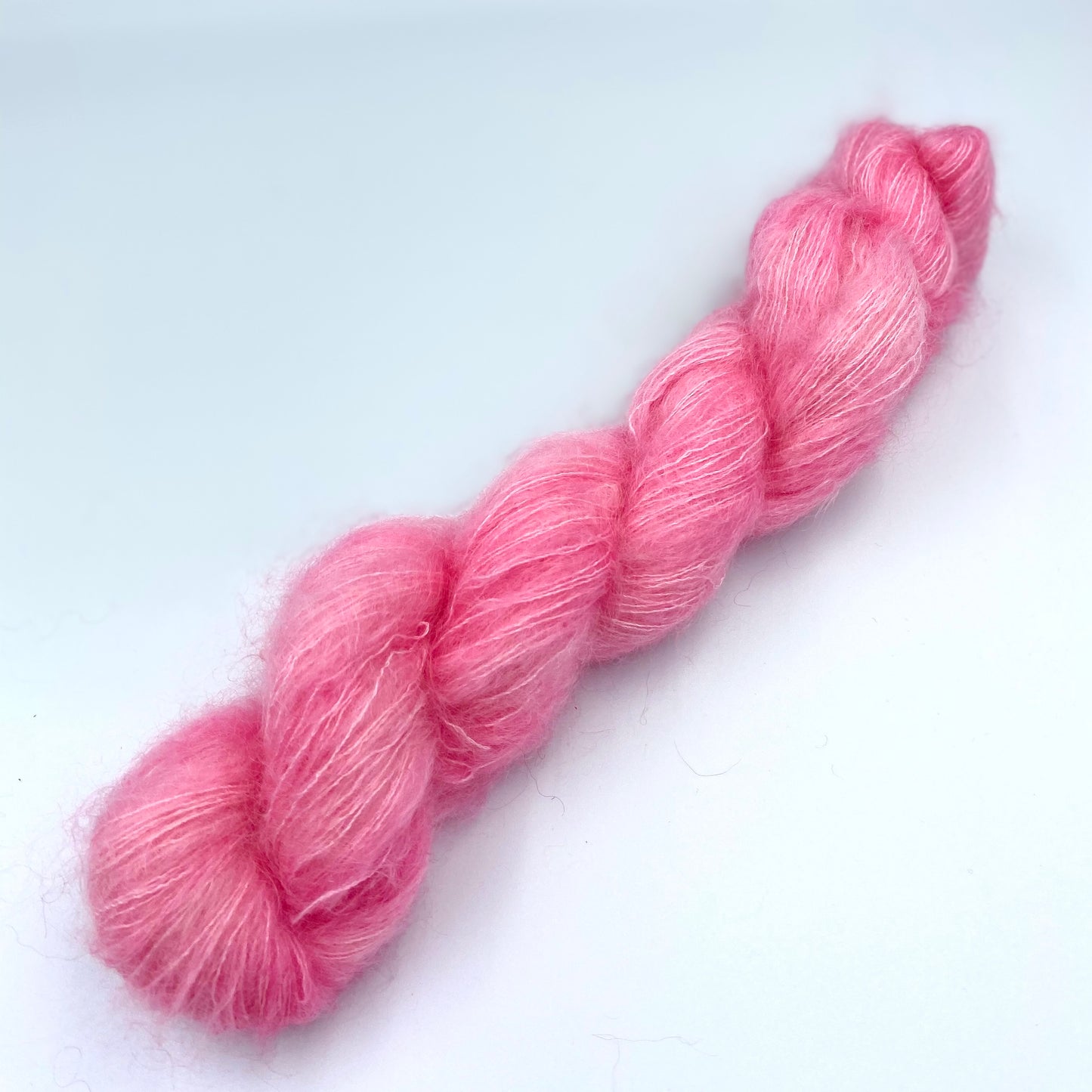 A skein of hand dyed kid mohair and silk yarn in a baby pink  color 