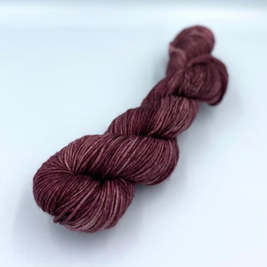 Skein of superwash merino yarn hand dyed in a red plum color