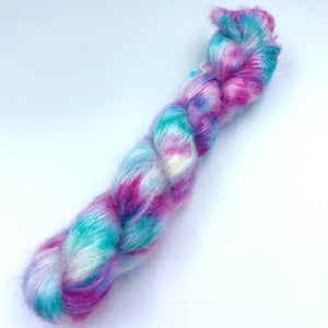 A skein of hand dyed kid mohair and silk yarn in a mix of turquoise, pink, purple splashed on a white base